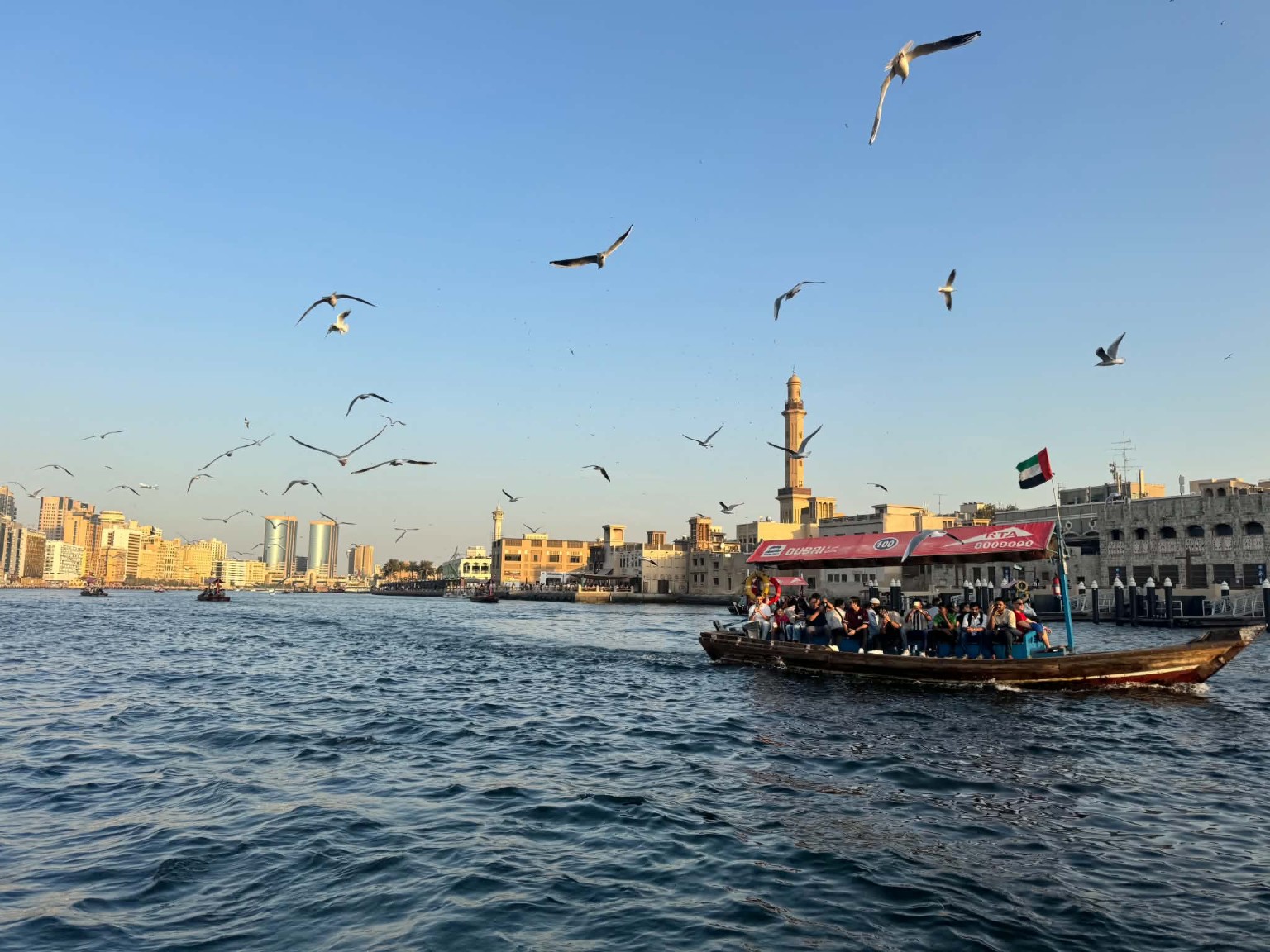 Traditional abra crossing Dubai Creek with the UAE flag and historic waterfront